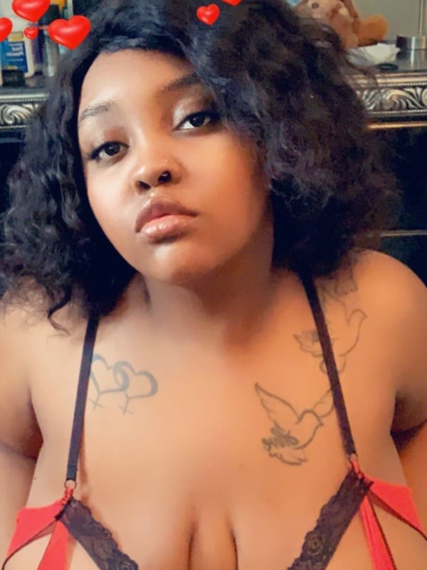 A woman with curly black hair wearing a red lace top and heart filters, posing confidently in front of a bathroom mirror.