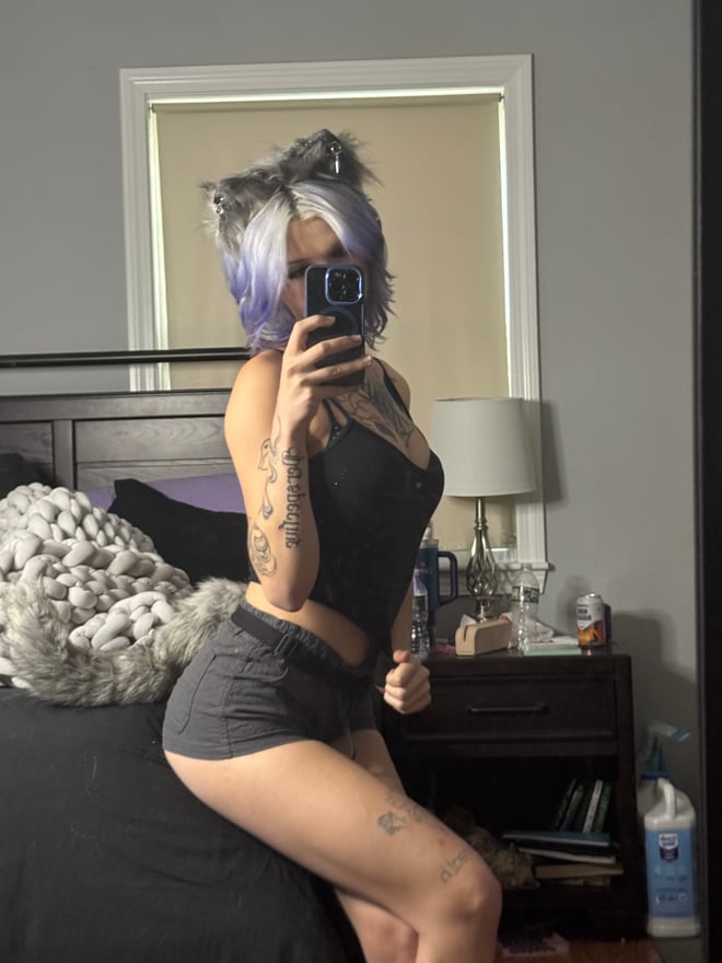 A person with blue hair poses indoors in a dark, distressed sweater layered over a black outfit.