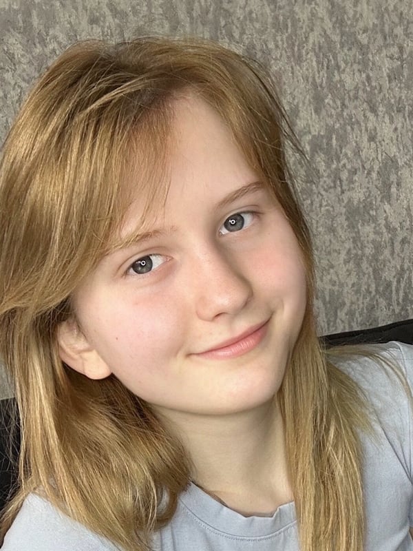 Close-up portrait of a young woman with blonde hair and blue eyes smiling gently while wearing a light-colored top.