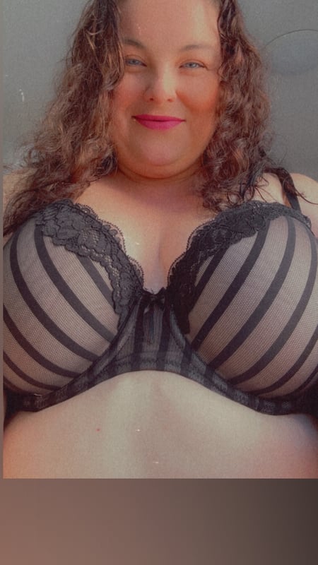 A woman with curly hair smiling confidently while wearing a striped lace top against a plain background.
