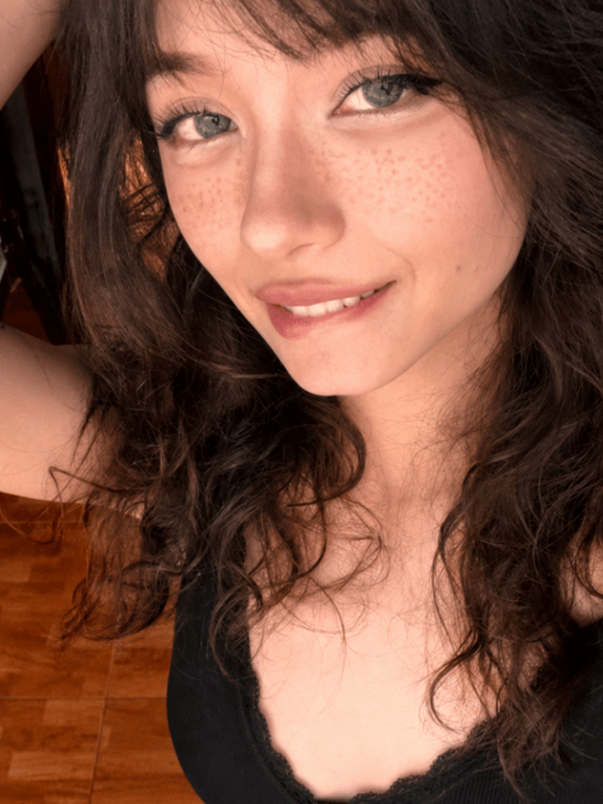 A person wearing a cat-ear headband and glasses, posing playfully while wearing a black outfit.