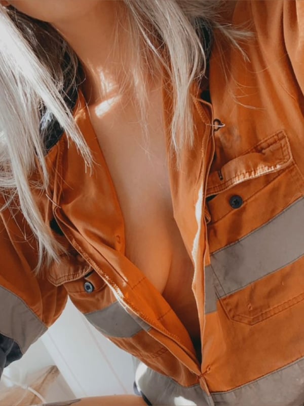A woman with long blonde hair wearing an open orange work shirt, smiling at the camera.