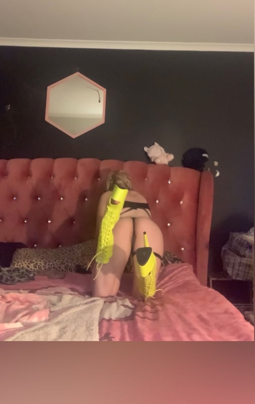 A person lounging on a pink bed in a stylish room with yellow arm sleeves and a mirror in the background.