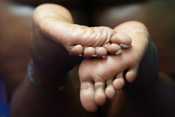 Close-up view of bare feet crossed together with painted toenails and a bracelet on the ankle.