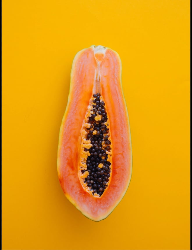 A fresh papaya fruit sliced open on a bright yellow background.