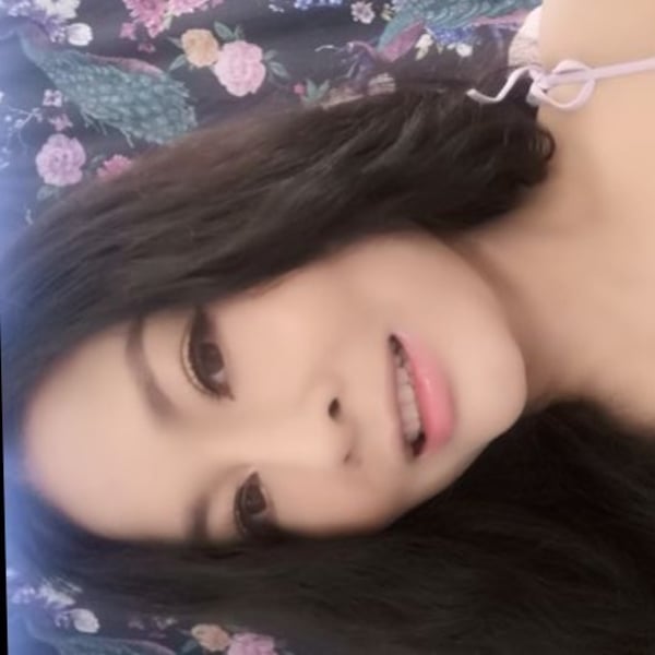 A woman with long dark hair smiling at the camera while lying on a colorful floral blanket.