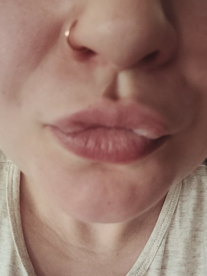 Close-up portrait of a woman with a nose piercing, full lips, and fair skin, making a playful expression.