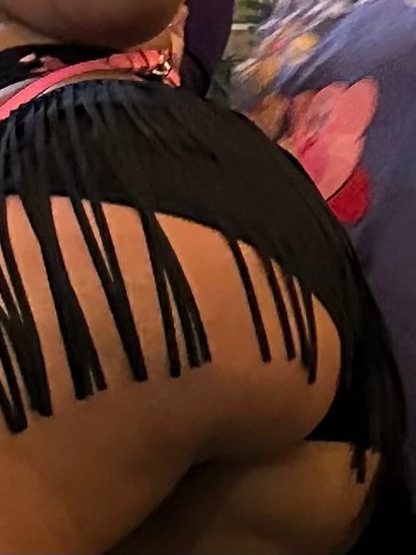 A close-up view of a woman's curvaceous figure in fringe black bottoms and colorful accessories against a purple background.