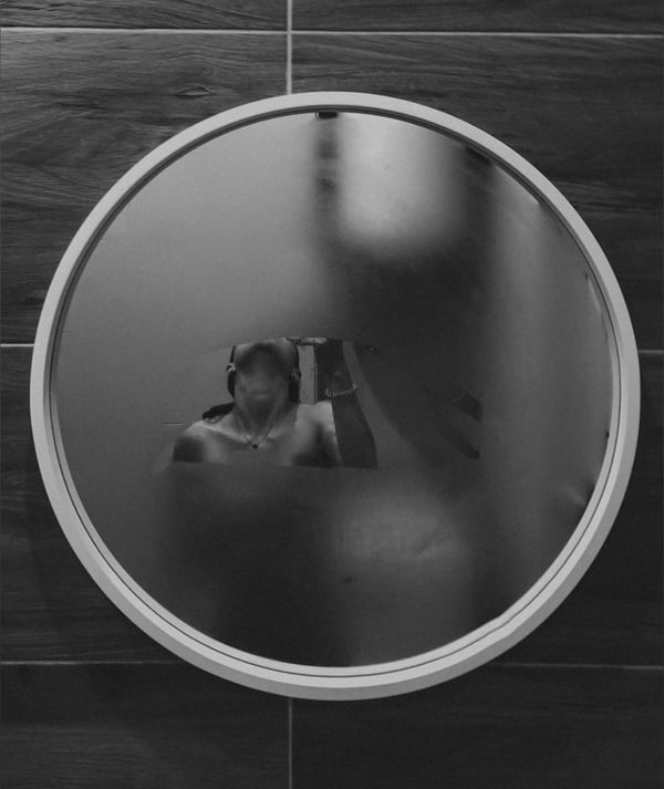 Reflective image of a person in a bathroom mirror with tiled walls.