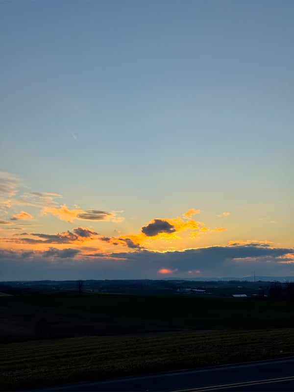 Scenic sunset over a rural landscape with fields and a road under a cloudy sky.