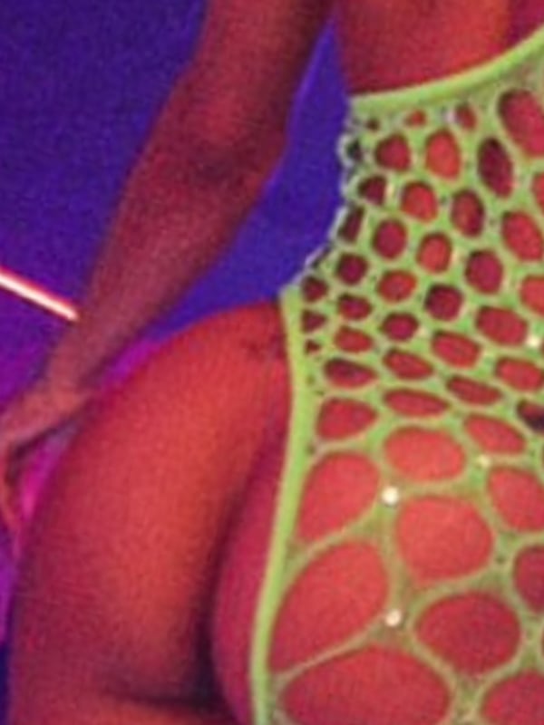 A woman in a green mesh outfit posing from behind in a neon-lit environment.