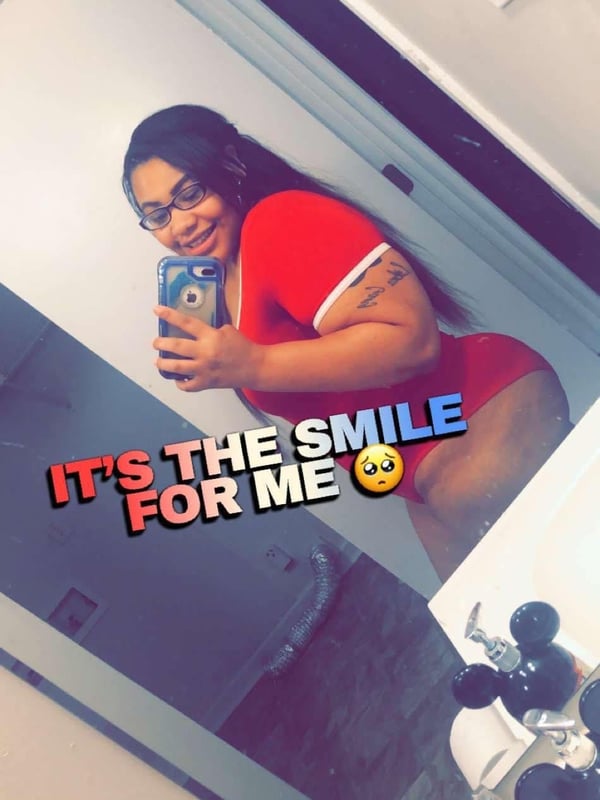 A woman smiling at the mirror selfie in a red top, with text overlay emphasizing her smile, in a bathroom setting.