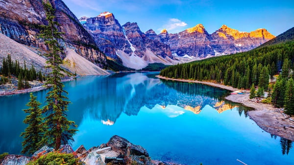 Scenic landscape featuring majestic snow-capped mountains surrounding a vibrant turquoise lake with evergreen forests in the foreground.