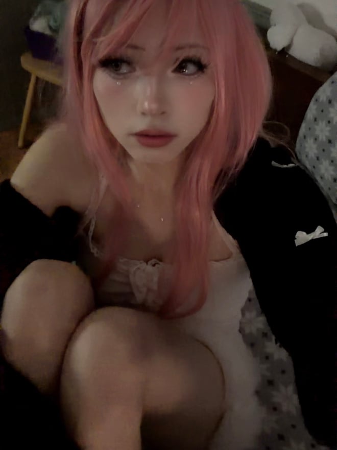 A person with pink hair posing indoors in a white ribbon-themed outfit.