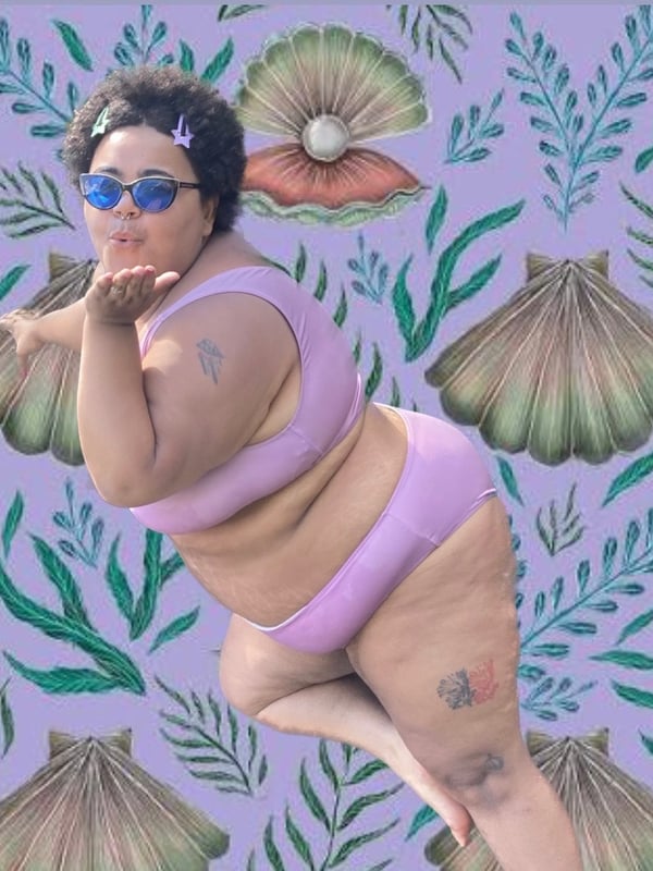 A smiling woman with sunglasses and curly hair posing playfully with a kiss gesture, wearing a pink bikini against a purple seashell and seaweed patterned background.