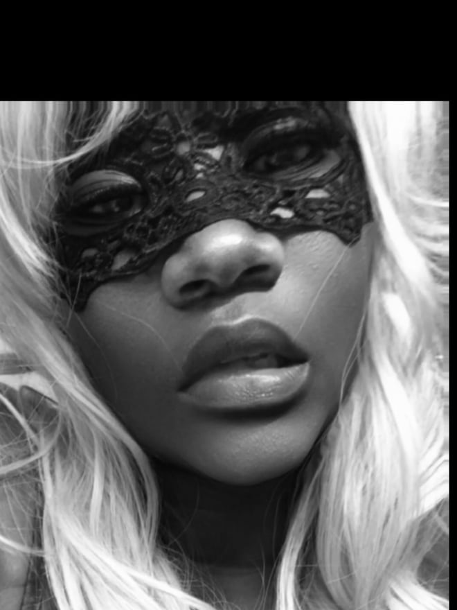 Close-up portrait of a woman wearing a black lace mask and long blonde hair, in black and white.