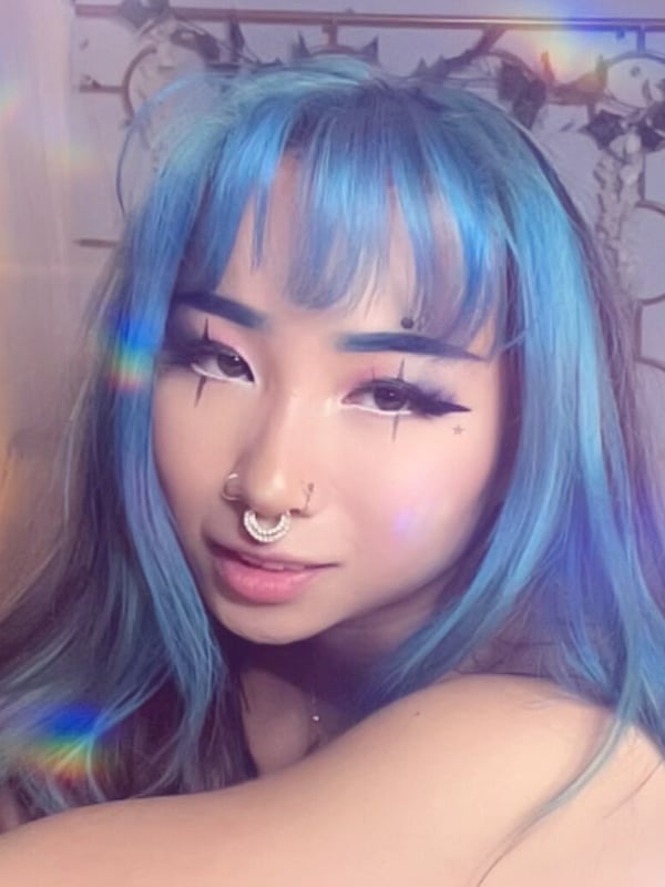 A close-up selfie of a person with bright blue hair and facial piercings.