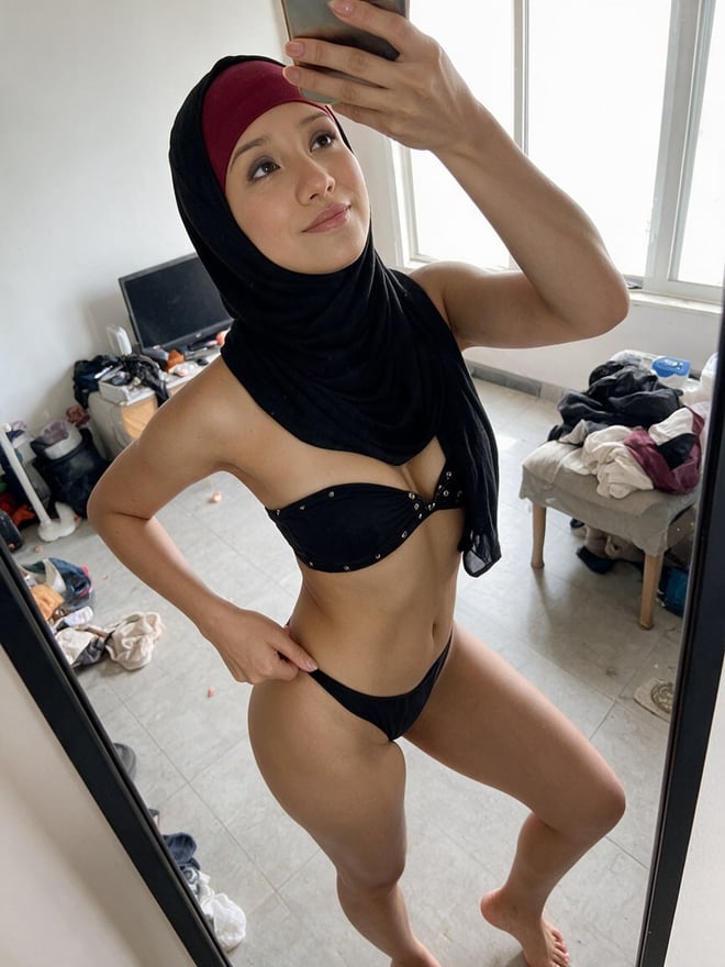 A close-up selfie of a woman wearing a hijab, posing indoors with her hand near her face.