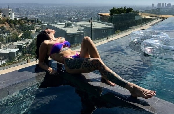 A woman in a purple bikini lounging by an infinity pool with a city skyline view in the background.