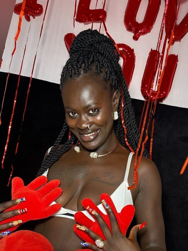 A woman smiling in front of a 'I LOVE YOU' balloon display with red heart decorations.