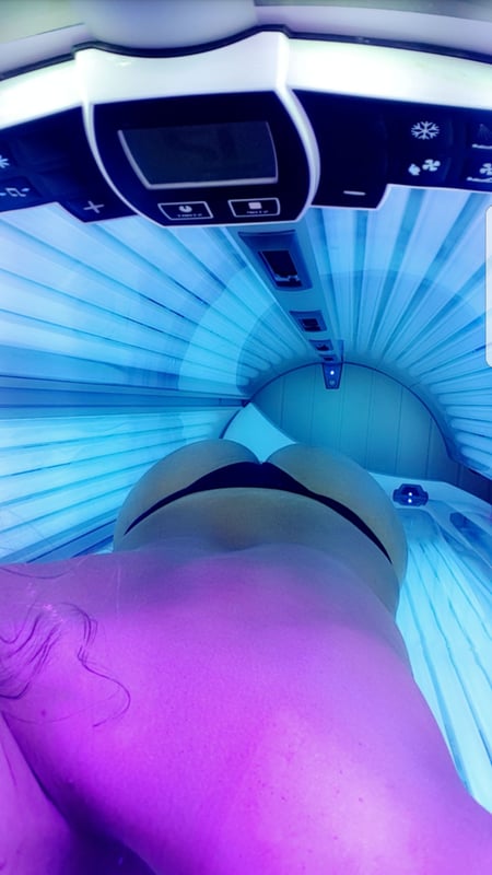 A person lying in a tanning bed with blue glowing lights, viewed from an overhead angle.