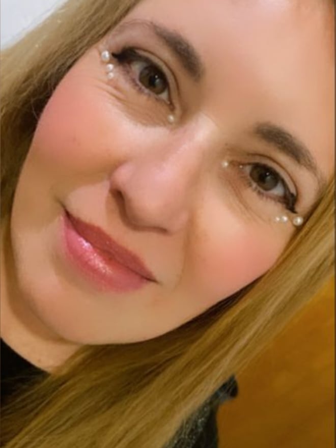 Close-up portrait of a woman with blonde hair, subtle makeup, and sparkling eye details, smiling softly against a neutral background.