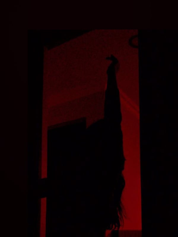 A silhouette of a woman with long hair posing in a doorway with red lighting.
