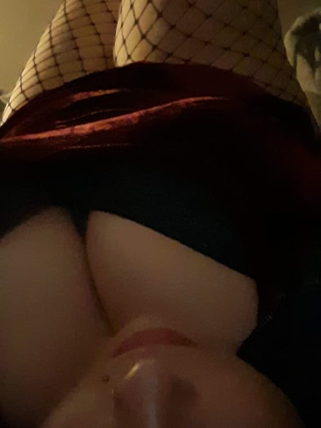 Overhead view of a woman lying down, showing her face and cleavage in a black top with fishnet stockings on her legs.