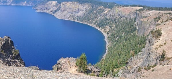 Scenic overlook of a deep blue lake surrounded by rocky cliffs and evergreen trees.