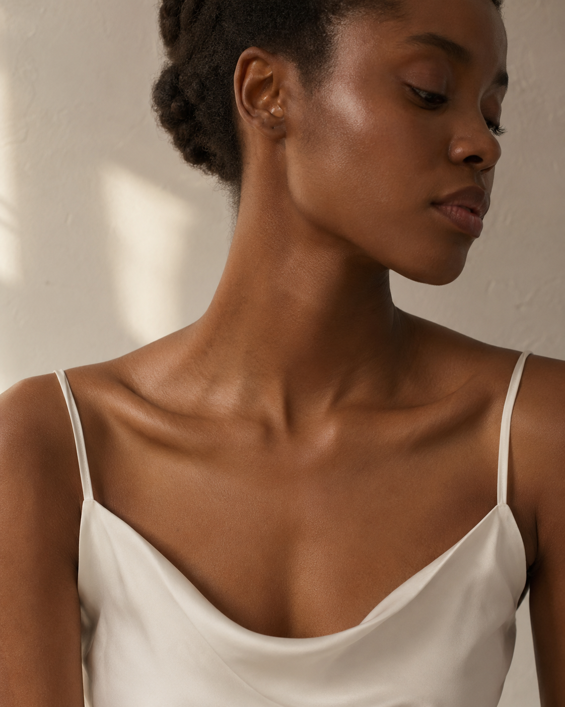 Editorial portrait of a Black woman in a neutral linen camisole, soft directional daylight across the décolletage and collarbone