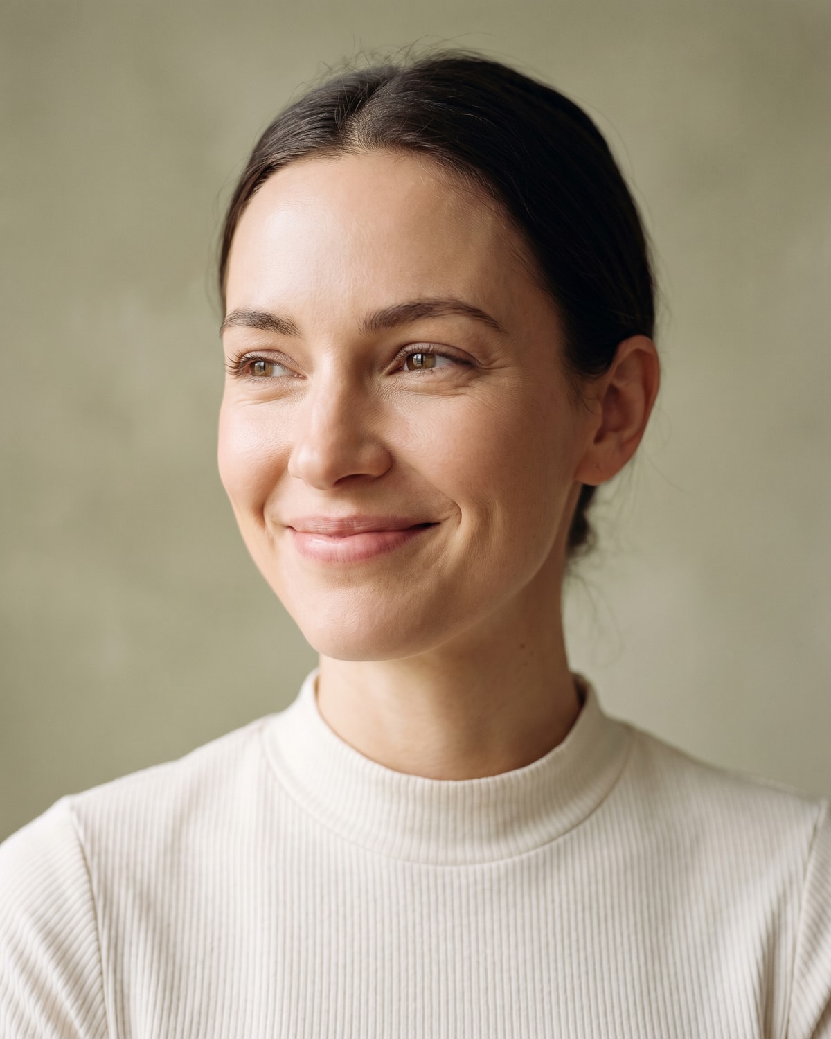 Woman laughing openly with her head tipped back in bright, almost shadowless light against a pale sage wall.