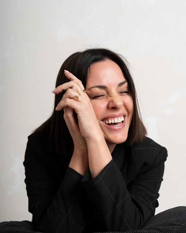 Close-up portrait, laughing warmly with one hand resting near the face