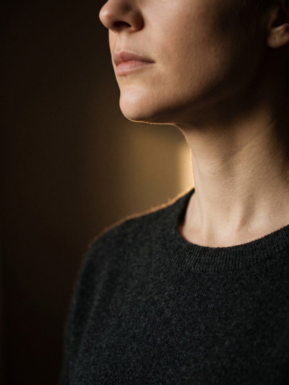 Wide crop of a jaw and neck, a single hard rim of light separating the jawline from deep shade behind it