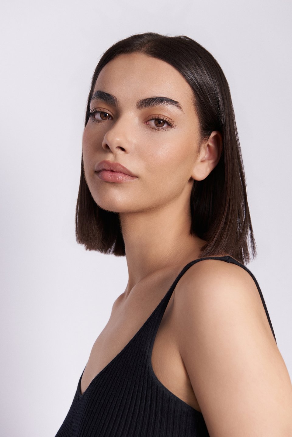 Editorial headshot of a woman with a brown bob, neutral natural makeup, gazing forward against a soft neutral backdrop