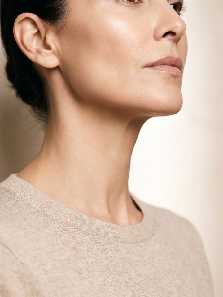 Jawline and neck in three-quarter view under broad front window light, the contour of the jaw reading cleanly against a warm bone wall.