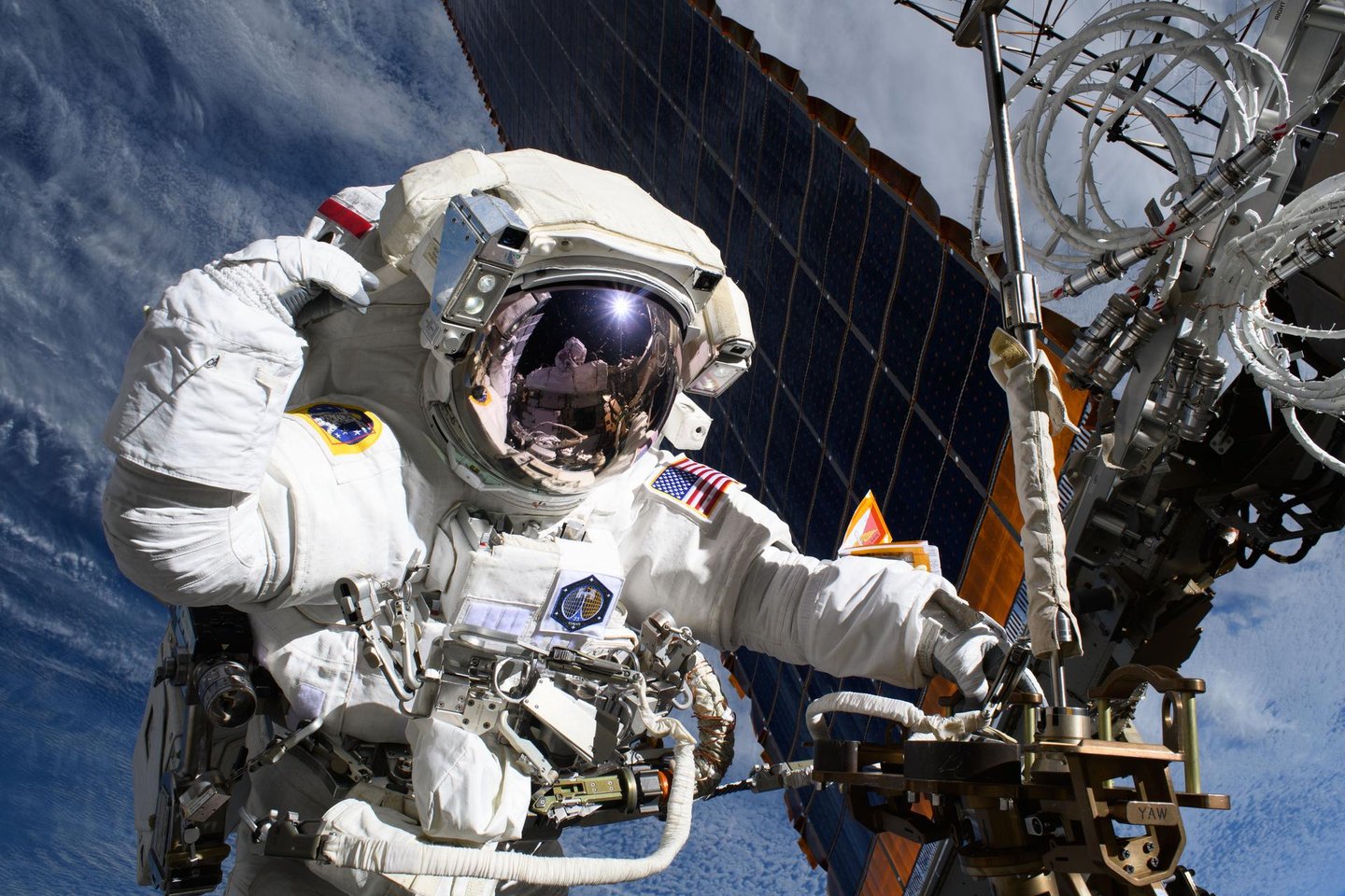 NASA astronotu Anne McClain, arkasında görülen ana güneş panelleri de dahil olmak üzere Uluslararası Uzay İstasyonu'nun güç üretim sistemlerini geliştirmek için bir uzay yürüyüşü gerçekleştiriyor.