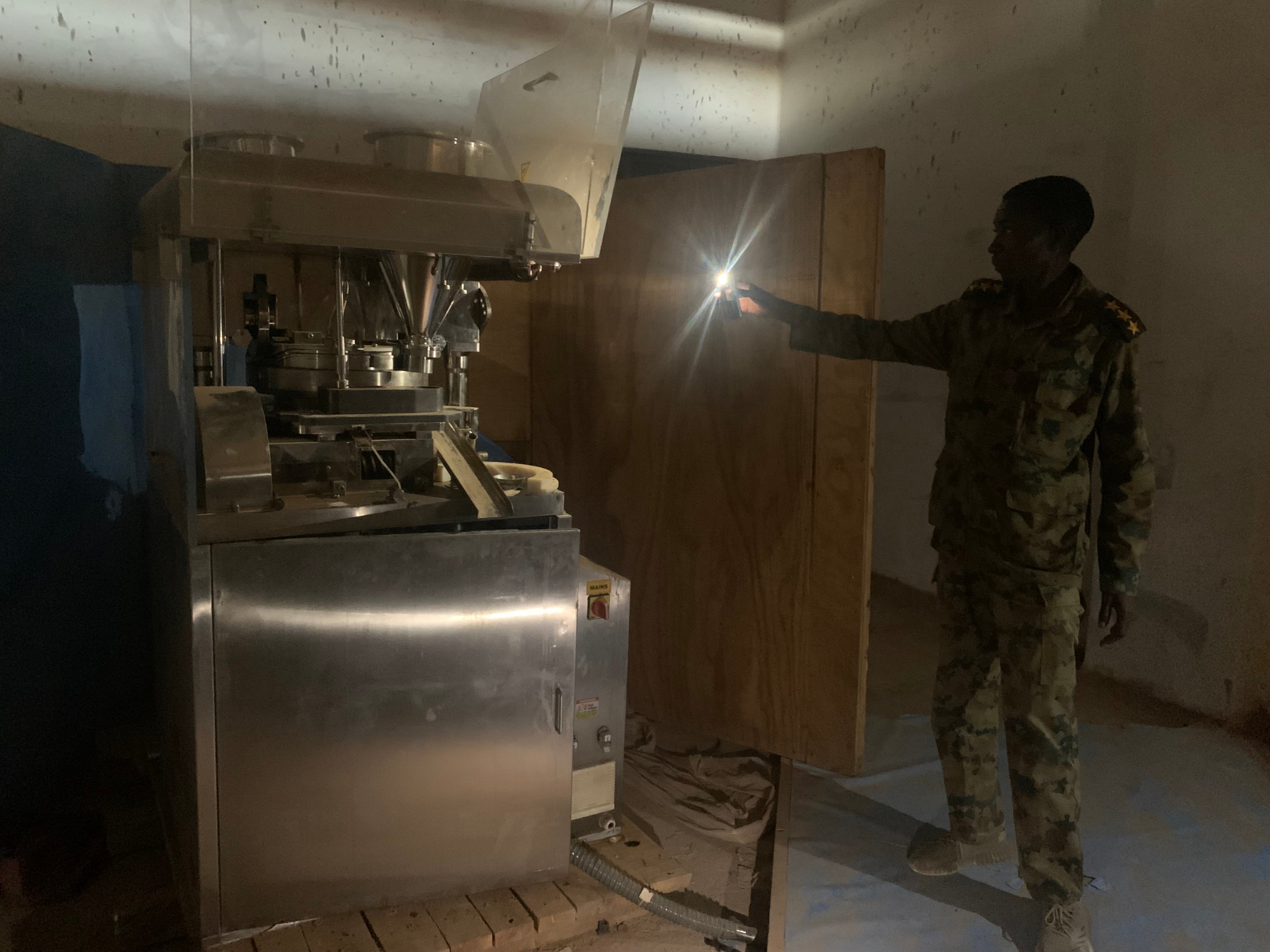 A soldier illuminates machinery to make pills at an abandoned building in Bahri on May 29; police said there were enough materials there to make 700 million Captagon pills. Residents said increasing narcotics use among RSF fighters had made them more violent and unpredictable. (Katharine Houreld/The Washington Post)