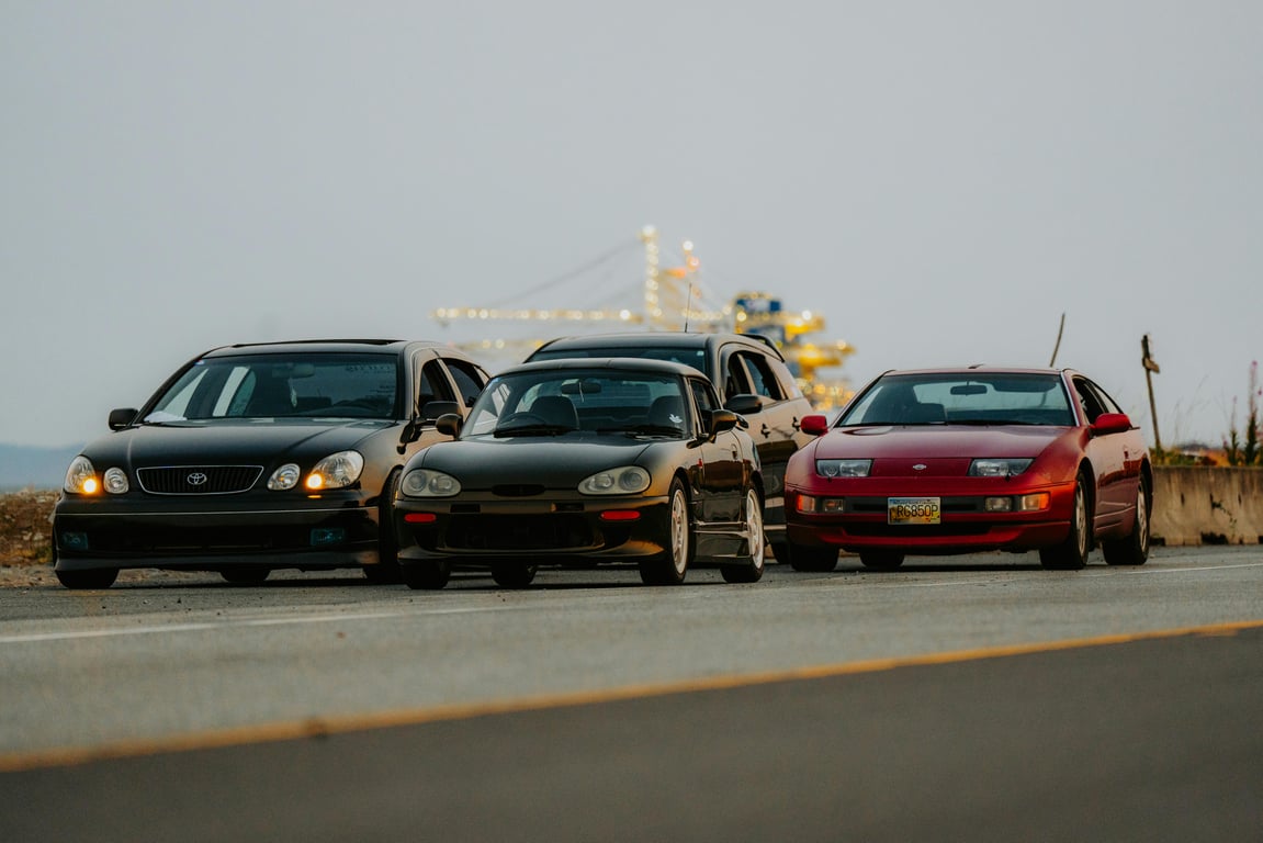 Four classic sports cars line up on a scenic road, ready for adventure.