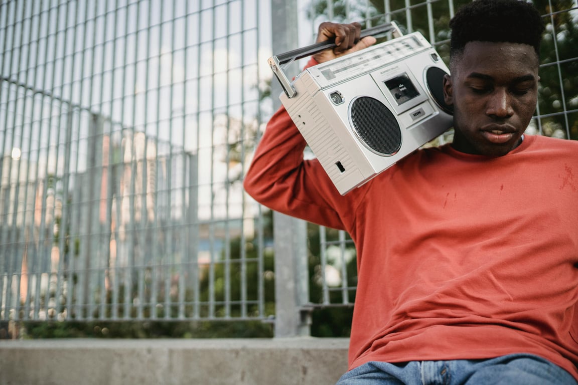 Young African American male in casual outfit sitting in park with boombox and listening to music