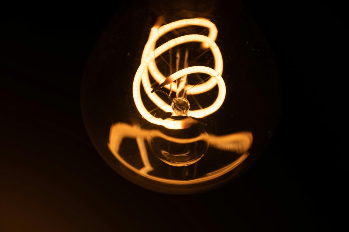 A close-up shot of an intricately illuminated vintage light bulb filament, glowing in the dark.