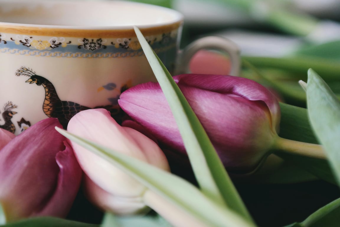 Elegant arrangement of purple tulips alongside a decorative porcelain cup, showcasing vibrant spring colors.