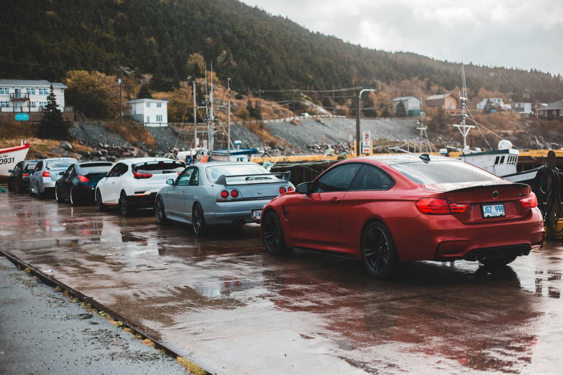 A lineup of modified sports cars parked on a wet pavement in a coastal town, evoking an adventurous mood.
