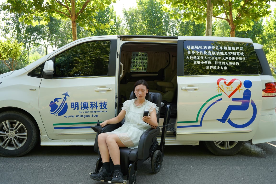 Asian woman using a smartphone in a wheelchair next to a modified van for accessibility.
