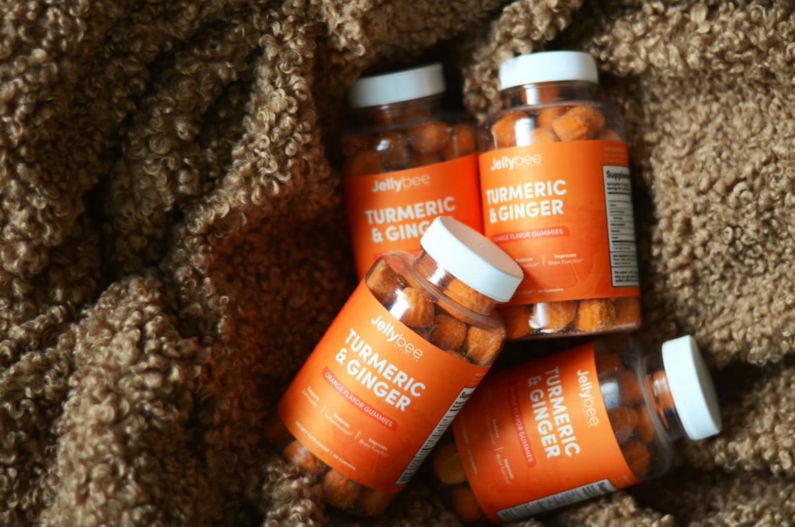 Four bottles of turmeric and ginger gummies set against a textured brown fabric backdrop.