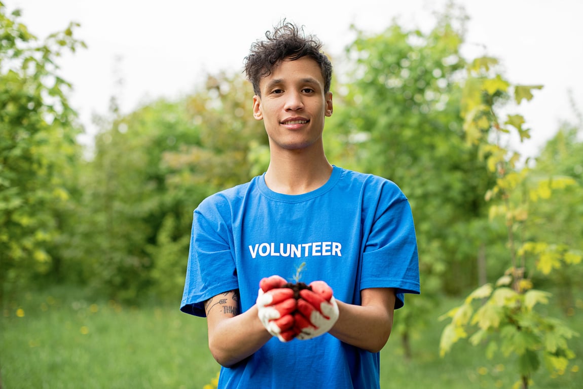 A young male volunteer holding a seedling, promoting environmental conservation.