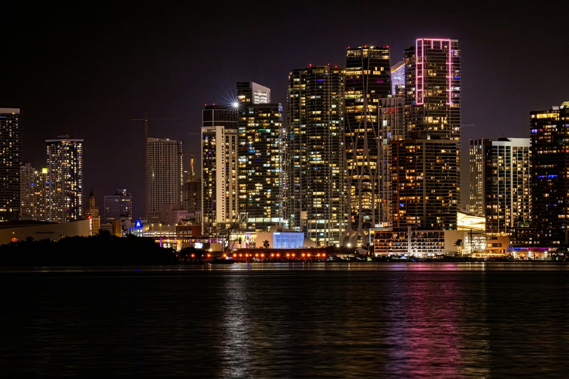 Vibrant Miami skyline illuminated at night, reflecting in the tranquil water.