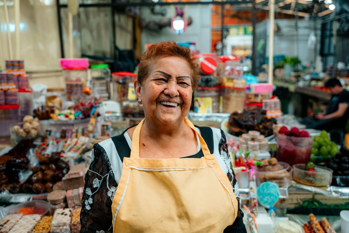 Smiling woman vendor at a lively indoor market surrounded by colorful merchandise.