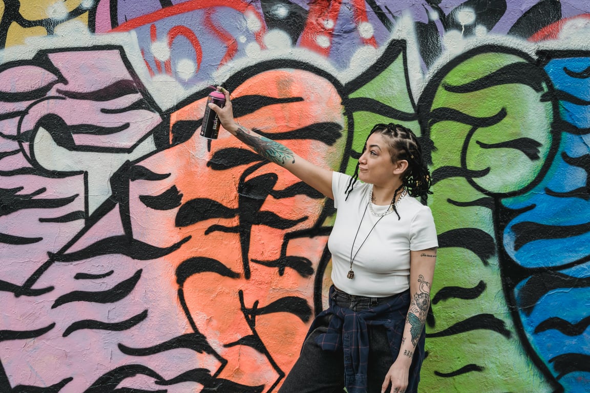 A woman artist paints a colorful graffiti mural on an urban wall, showcasing creativity.