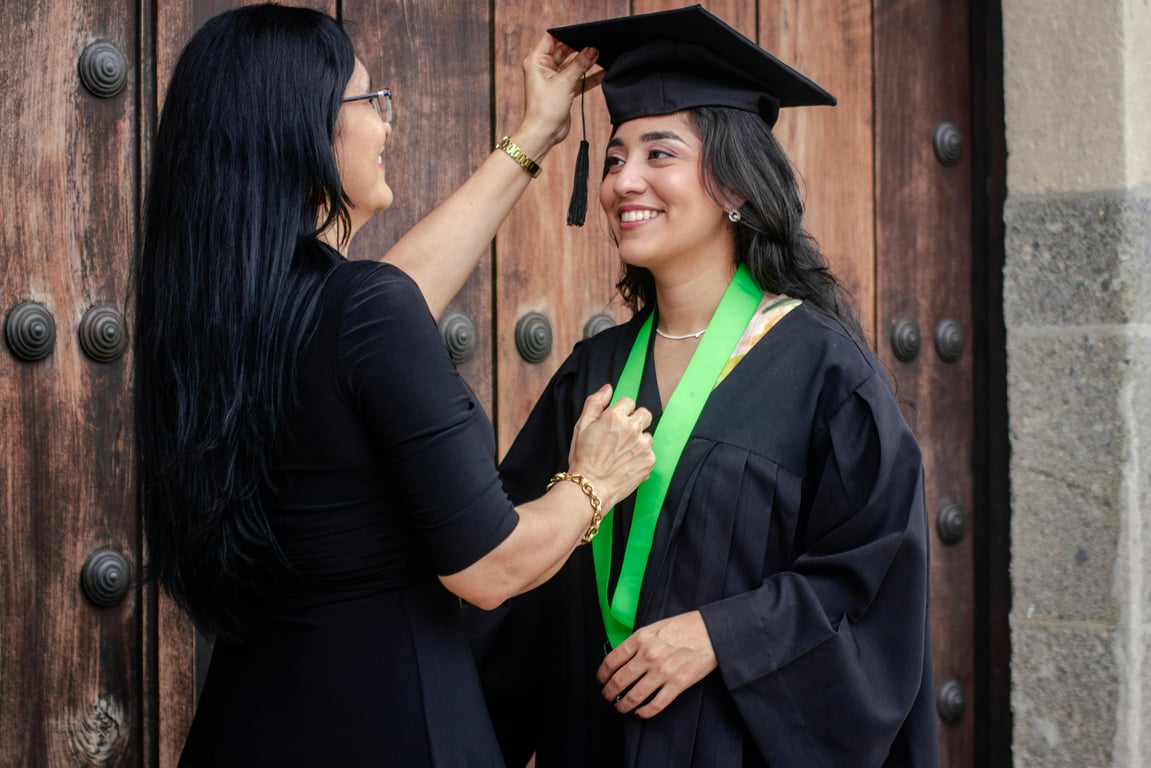 A joyful moment as a mother adjusts her daughter's graduation cap on a sunny day.