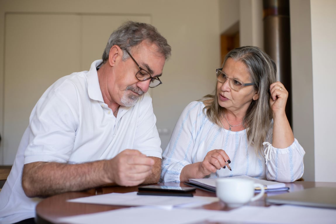 Senior couple reviewing documents and managing finances together at home, showing collaboration and care.